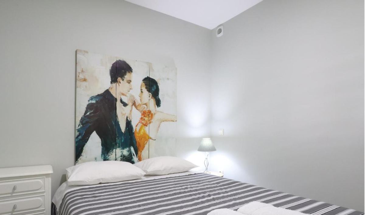 Quarto com cama de casal, cómoda branca e um quadro de dois dançarinos na parede